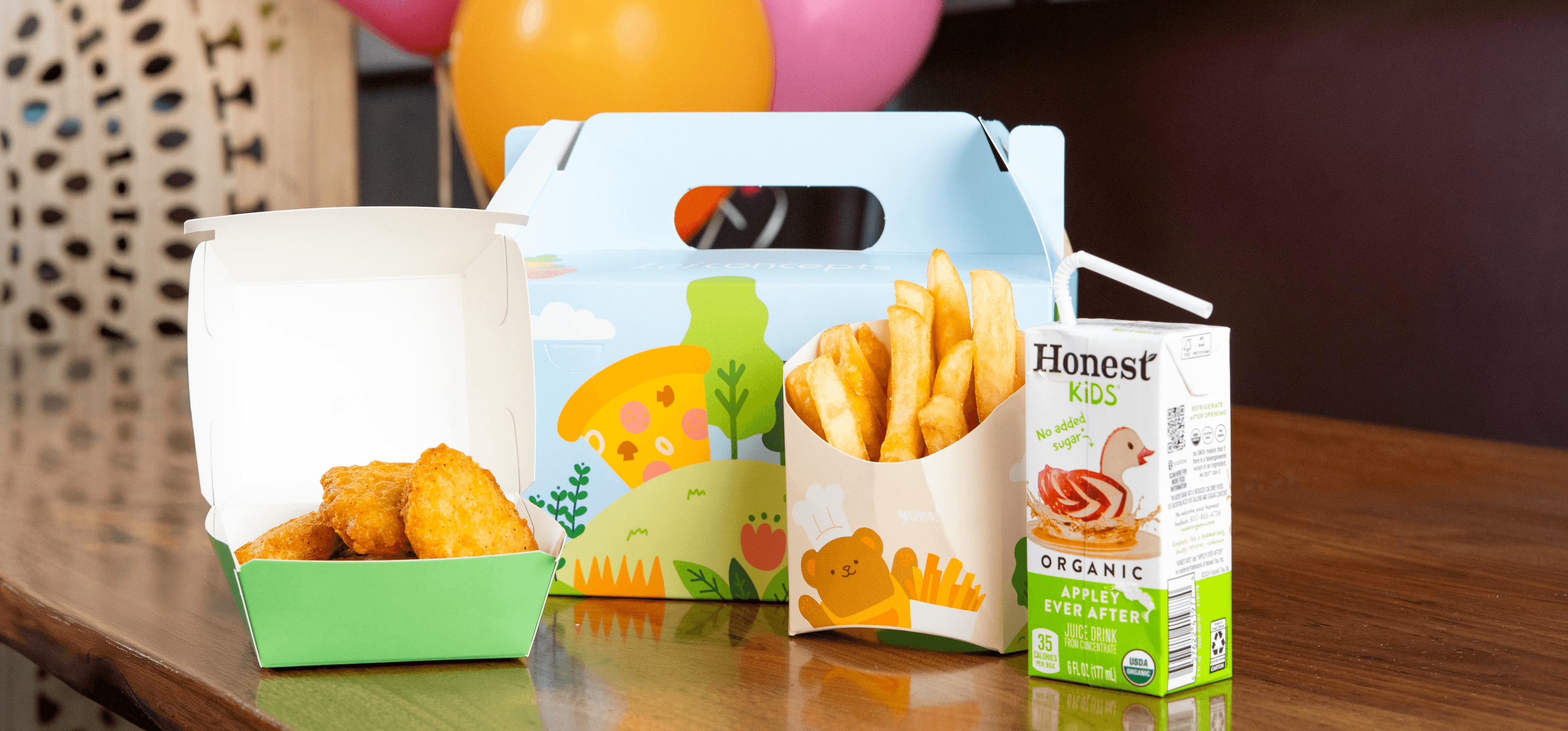 A colorful kids meal box featuring chicken nuggets, fries, and an organic apple juice box, highlighting Kei Concepts’ family-friendly dining experience for children and families.