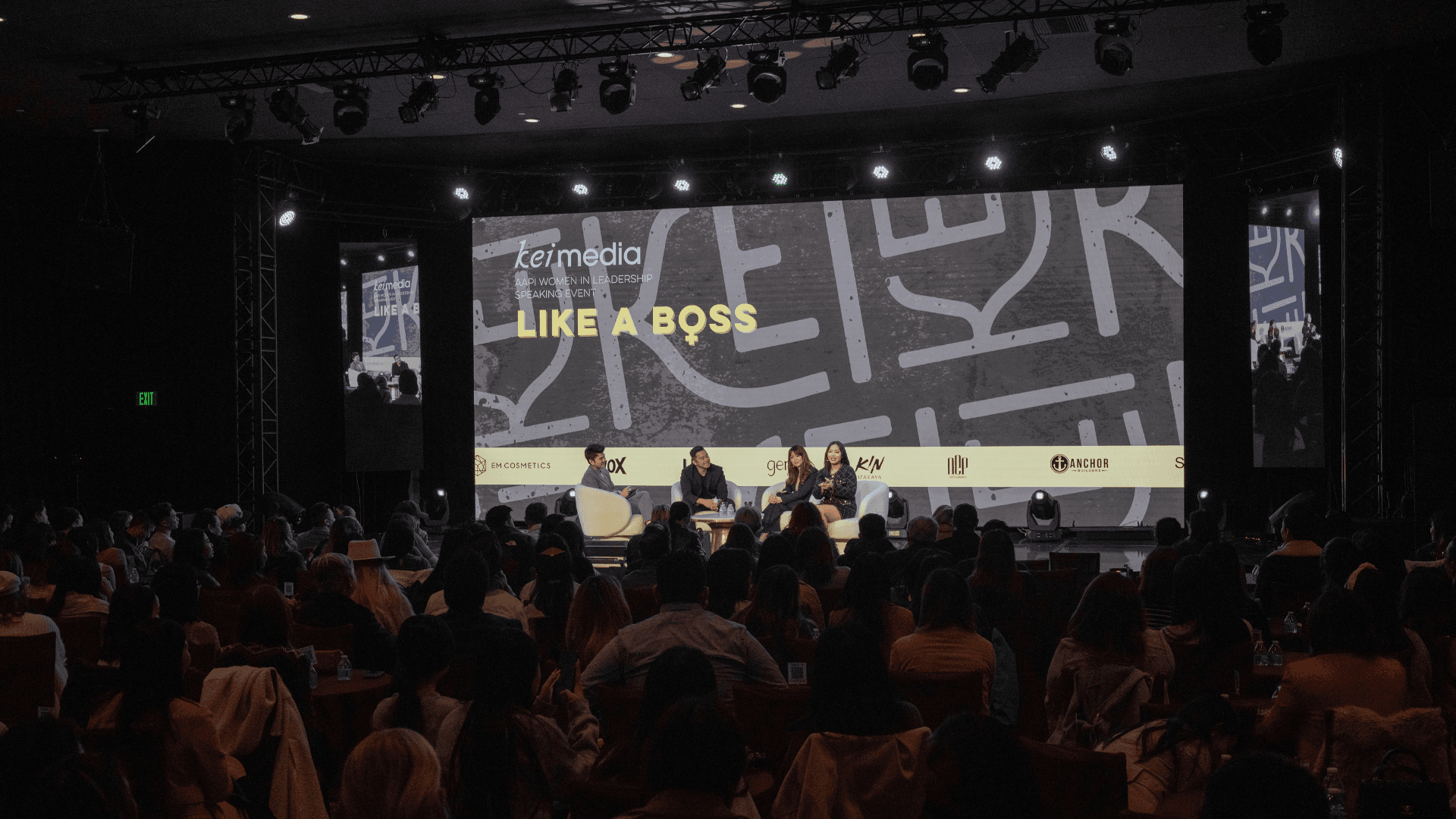 Audience attending a Kei Media live event featuring a panel discussion on stage beneath a large “Like a Boss” presentation screen, with speakers seated in front of a packed conference crowd.