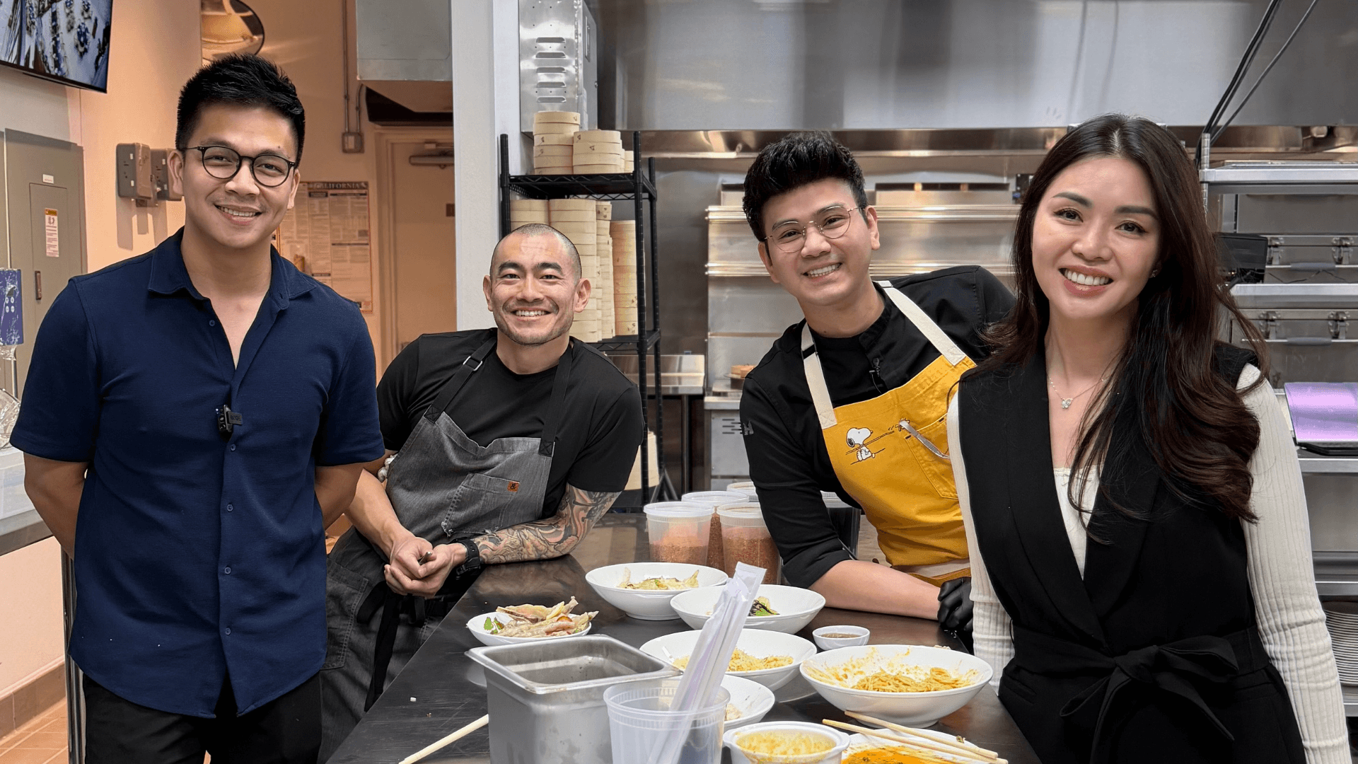 Portrait of founders Neo Du, Edward Huang, Viet Nguyen, and Ivy Ha smiling together inside a professional restaurant kitchen, standing beside plated dishes and cooking stations.